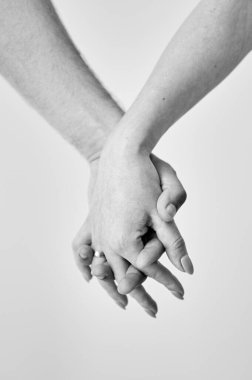 Tarafsız bir arkaplanda iki el bir arada tutuldu. Erkek ve kadın elinin yakınına. Samimiyet, destek ve güven kavramı. Siyah ve beyaz resim.