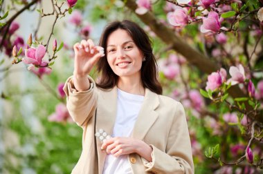Bahar mevsimsel alerjisi olan kadın alerjisi. Alerji ilacı gösteren mutlu genç bir kadın baharda çiçek açan bahçede poz veriyor. Antihistamin ilaç konsepti