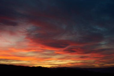Göz kamaştırıcı günbatımı gökyüzünü kırmızı, turuncu ve pembe renkleriyle boyar. Derin maviler ve morlar ile harmanlanır. Siluetli tepeler, ateşli ufka karşı tezat oluşturarak, huzurlu manzaraya dram katıyor..