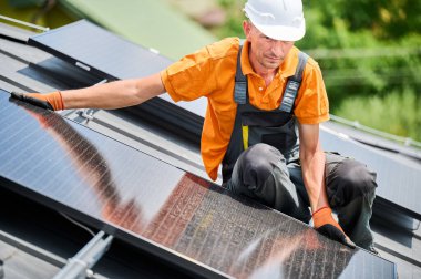 Evin çatısına güneş paneli inşa eden bir işçi. Dışarıda fotovoltaik güneş modülü kuran miğferdeki adam mühendis. Alternatif, yeşil ve yenilenebilir enerji üretimi kavramı.