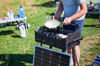 Yakından bakınca, fırının üzerinde ızgaranın üzerinde altın sarısı krep pişiriyor. Güneşli çimenlik alanda sahne.