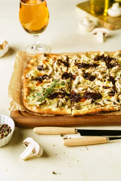 Homemade Belgian style mushroom pizza, flammekeuche, on wooden board, wine and beer in glasses on light colored background, vertical image