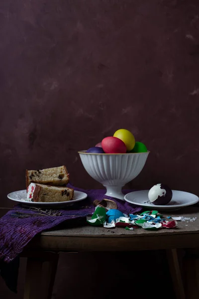 Martwa natura z plasterkami ciasta wielkanocnego, kolorowymi jajkami i skorupkami jaj na rustykalnym tle — Zdjęcie stockowe