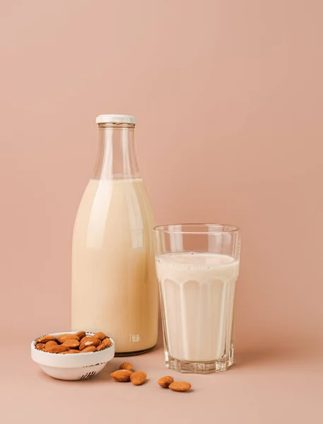 Plant based almond milk in bottle and glass on pink background. Portrait orientation