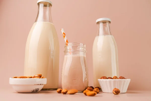 Various vegan plant based milk and ingredients. Dairy free milk substitute drinks on pink background, closeup view. Horizontal orientation