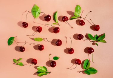 Mercan pembe zemin üzerinde yaprak ve saplı tatlı kirazlar, üst manzara.