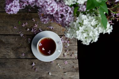 Bir fincan siyah çay, ahşap kırsal masada bir buket leylak çiçeği, üst manzara. Yatay resim