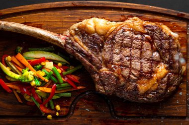 Tomahawk steak and veggies on a serving board. Low key image, horizontal orientation clipart