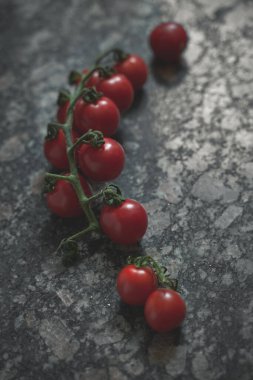 Granit arka plandaki dallarda kiraz domatesleri, yakın görüş, seçici odaklanma. Portre yönelimi