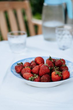 Bahçe masasındaki tabakta taze çilekler kahvaltıda servis ediliyor, yakın çekim görüntüsü.