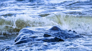 Dalgalar kıyıya vurur ve kayalara çarpar. Kıyıya yakın yerlerde bir sürü sıçrama ve sıçrama meydana getirir. Taştan çakıl taşı kıyısında dalgalı köpüklü dalgalarla fırtınalı havada nehir sörfü yapmak..