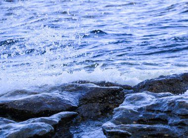Dalgalar kıyıya vurur ve kayalara çarpar. Kıyıya yakın yerlerde bir sürü sıçrama ve sıçrama meydana getirir. Taştan çakıl taşı kıyısında dalgalı köpüklü dalgalarla fırtınalı havada nehir sörfü yapmak..