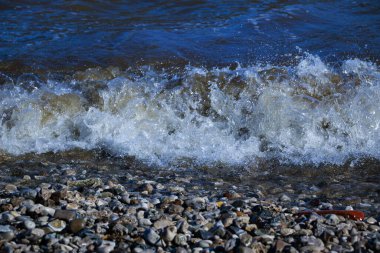 Dalgalar kıyıya doğru koşar ve kayalara çarpar. Kıyıya yakın yerlerde bir sürü sıçrama ve sıçrama meydana getirir. Fırtınalı havada, köpüklü dalgalarla taştan bir çakıl taşı kıyısında sörf yapan nehir..