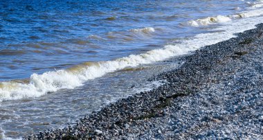 Dalgalar kıyıya doğru koşar ve kayalara çarpar. Kıyıya yakın yerlerde bir sürü sıçrama ve sıçrama meydana getirir. Fırtınalı havada, köpüklü dalgalarla taştan bir çakıl taşı kıyısında sörf yapan nehir..
