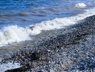 Dalgalar kıyıya doğru koşar ve kayalara çarpar. Kıyıya yakın yerlerde bir sürü sıçrama ve sıçrama meydana getirir. Fırtınalı havada, köpüklü dalgalarla taştan bir çakıl taşı kıyısında sörf yapan nehir..