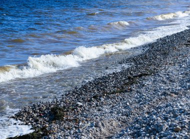 Dalgalar kıyıya doğru koşar ve kayalara çarpar. Kıyıya yakın yerlerde bir sürü sıçrama ve sıçrama meydana getirir. Fırtınalı havada, köpüklü dalgalarla taştan bir çakıl taşı kıyısında sörf yapan nehir..