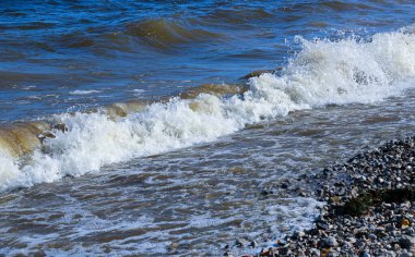 Dalgalar kıyıya doğru koşar ve kayalara çarpar. Kıyıya yakın yerlerde bir sürü sıçrama ve sıçrama meydana getirir. Fırtınalı havada, köpüklü dalgalarla taştan bir çakıl taşı kıyısında sörf yapan nehir..
