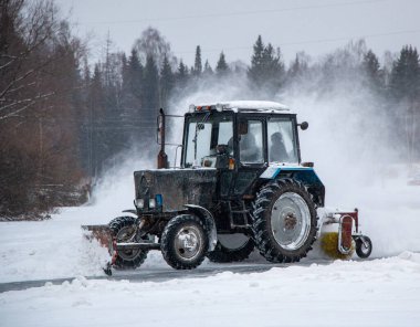 Karla kaplı eski bir traktör yolu karla kaplıyor, yolu karla süpürüyor, büyük bir çalıyla, şiddetli bir kar fırtınasıyla..