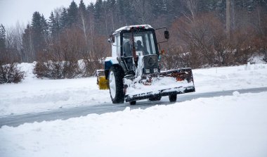 Karla kaplı eski bir traktör yolu karla kaplıyor, yolu karla süpürüyor, büyük bir çalıyla, şiddetli bir kar fırtınasıyla..