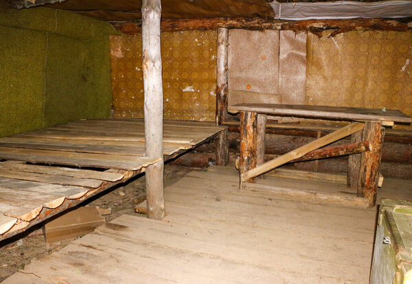 старые военные раскопки в лесу с окопами, выложенными и укрепленными бревнами и маленькими землянками и убежищами, построенными из древесных материалов, бревен и досок, под землей.