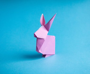 Mavi arkaplandaki renkli kağıttan bir origami tavşanı yaratmak için adım adım talimatlar, dekoratif bir Paskalya partisi süsü ya da küçük Paskalya hediyeleri için.