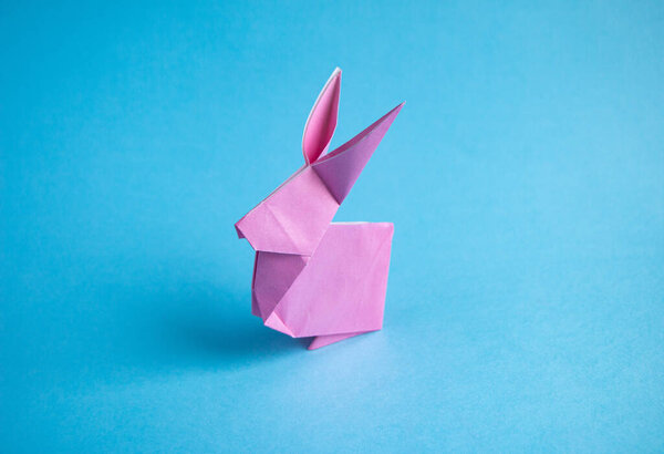 Пошаговые инструкции по созданию кролика оригами из цветной бумаги на синем фоне, для декоративного украшения пасхальной вечеринки или для маленьких пасхальных подарков.