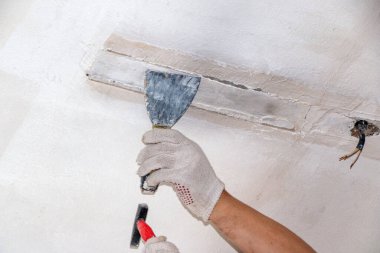mans hand in a cloth glove with a spatula and putty, applies mastic to wall, ceiling to level  surface. process of applying mastic with a spatula to surface for interior design of the room.  clipart