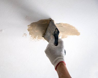 Erkekler spatula ve macunla birlikte kumaş eldiveni veriyorlar, mastiği duvara, tavanı da yüzeye uyguluyorlar. Odanın iç tasarımı için bir spatula ile mastik uygulanması süreci. 