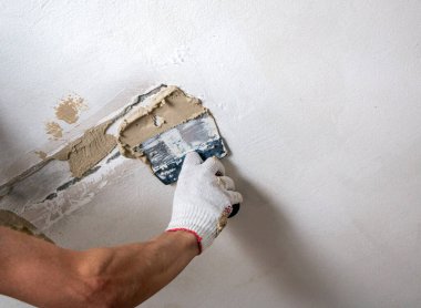 Erkekler spatula ve macunla birlikte kumaş eldiveni veriyorlar, mastiği duvara, tavanı da yüzeye uyguluyorlar. Odanın iç tasarımı için bir spatula ile mastik uygulanması süreci. 