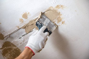 Erkekler spatula ve macunla birlikte kumaş eldiveni veriyorlar, mastiği duvara, tavanı da yüzeye uyguluyorlar. Odanın iç tasarımı için bir spatula ile mastik uygulanması süreci. 