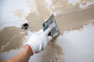 Erkekler spatula ve macunla birlikte kumaş eldiveni veriyorlar, mastiği duvara, tavanı da yüzeye uyguluyorlar. Odanın iç tasarımı için bir spatula ile mastik uygulanması süreci. 