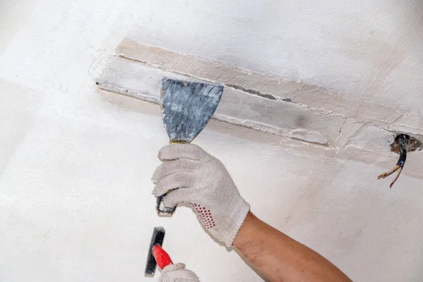 mans hand in a cloth glove with a spatula and putty, applies mastic to wall, ceiling to level  surface. process of applying mastic with a spatula to surface for interior design of the room.