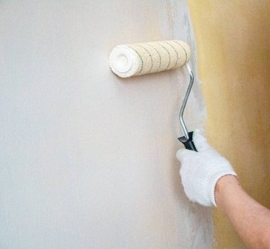 Eldivenli bir adam boya rulosuyla duvar yüzeyine yeni boya ve astar uygular. Odanın iç tasarımı için su bazlı boya ve boya silindirli astar kullanım süreci.