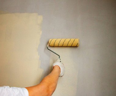 Eldivenli bir adam boya rulosuyla duvar yüzeyine yeni boya ve astar uygular. Odanın iç tasarımı için su bazlı boya ve boya silindirli astar kullanım süreci.