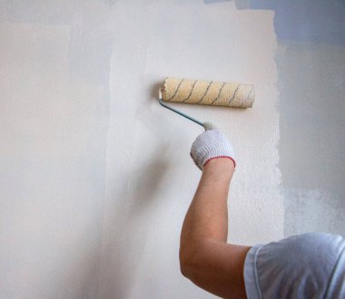 Eldivenli bir adam boya rulosuyla duvar yüzeyine yeni boya ve astar uygular. Odanın iç tasarımı için su bazlı boya ve boya silindirli astar kullanım süreci.
