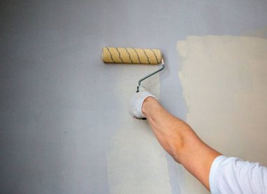 Eldivenli bir adam boya rulosuyla duvar yüzeyine yeni boya ve astar uygular. Odanın iç tasarımı için su bazlı boya ve boya silindirli astar kullanım süreci.