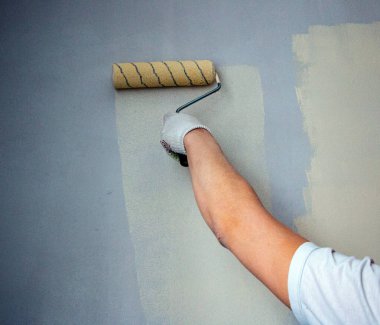 Eldivenli bir adam boya rulosuyla duvar yüzeyine yeni boya ve astar uygular. Odanın iç tasarımı için su bazlı boya ve boya silindirli astar kullanım süreci.