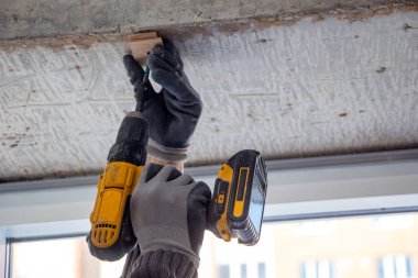 Bir inşaat işçisinin erkek elleri vidaları sıkılaştırır ve tamir eder ve kablosuz bir tornavidayla ev dekorasyonu ve iç dekorasyon için kendi kendine dokunur.. 