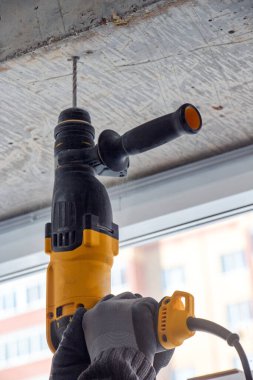 Bir inşaat işçisinin erkek eli elle matkapla betonda delik açar. Çarpışma matkabı kullanarak beton kirişlerde ve çapraz çubuklarda delik açma işlemi.