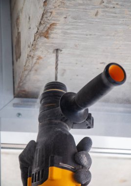 Bir inşaat işçisinin erkek eli elle matkapla betonda delik açar. Çarpışma matkabı kullanarak beton kirişlerde ve çapraz çubuklarda delik açma işlemi.