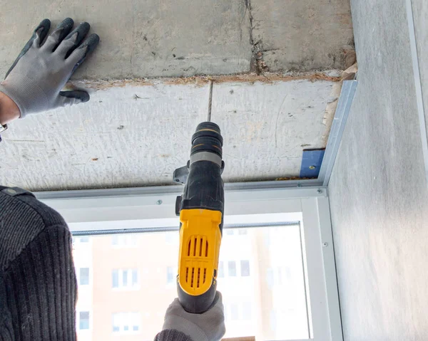 Bir inşaat işçisinin erkek eli elle matkapla betonda delik açar. Çarpışma matkabı kullanarak beton kirişlerde ve çapraz çubuklarda delik açma işlemi.