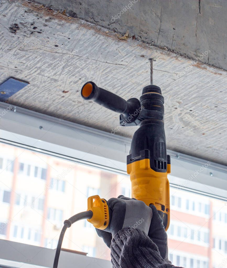 male hands of a construction worker drills a hole in concrete with a hand drill. the process of drilling holes in concrete beams and crossbar for various fastenings using an impact drill.