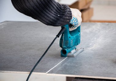 Bir inşaat işçisinin elleri elektrikli bir yapbozun parçalarını kesip biçiyor. İç dekorasyon için bir yapı tahtasını elektrikli bir yap-boz ile kesme işlemi