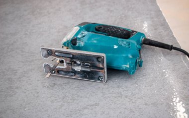 Bir inşaat işçisinin elleri elektrikli bir yapbozun parçalarını kesip biçiyor. İç dekorasyon için bir yapı tahtasını elektrikli bir yap-boz ile kesme işlemi