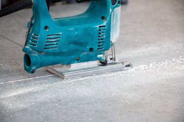 Bir inşaat işçisinin elleri elektrikli bir yapbozun parçalarını kesip biçiyor. İç dekorasyon için bir yapı tahtasını elektrikli bir yap-boz ile kesme işlemi