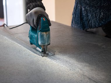 Bir inşaat işçisinin elleri elektrikli bir yapbozun parçalarını kesip biçiyor. İç dekorasyon için bir yapı tahtasını elektrikli bir yap-boz ile kesme işlemi