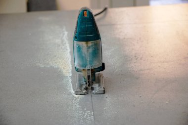 Bir inşaat işçisinin elleri elektrikli bir yapbozun parçalarını kesip biçiyor. İç dekorasyon için bir yapı tahtasını elektrikli bir yap-boz ile kesme işlemi