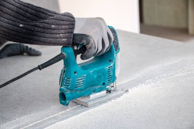 Bir inşaat işçisinin elleri elektrikli bir yapbozun parçalarını kesip biçiyor. İç dekorasyon için bir yapı tahtasını elektrikli bir yap-boz ile kesme işlemi