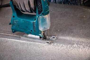 Bir inşaat işçisinin elleri elektrikli bir yapbozun parçalarını kesip biçiyor. İç dekorasyon için bir yapı tahtasını elektrikli bir yap-boz ile kesme işlemi