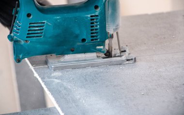 Bir inşaat işçisinin elleri elektrikli bir yapbozun parçalarını kesip biçiyor. İç dekorasyon için bir yapı tahtasını elektrikli bir yap-boz ile kesme işlemi